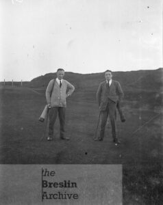Two men on the green with golf clubs.