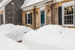 Piles of snow in front of a shingled Maine house.